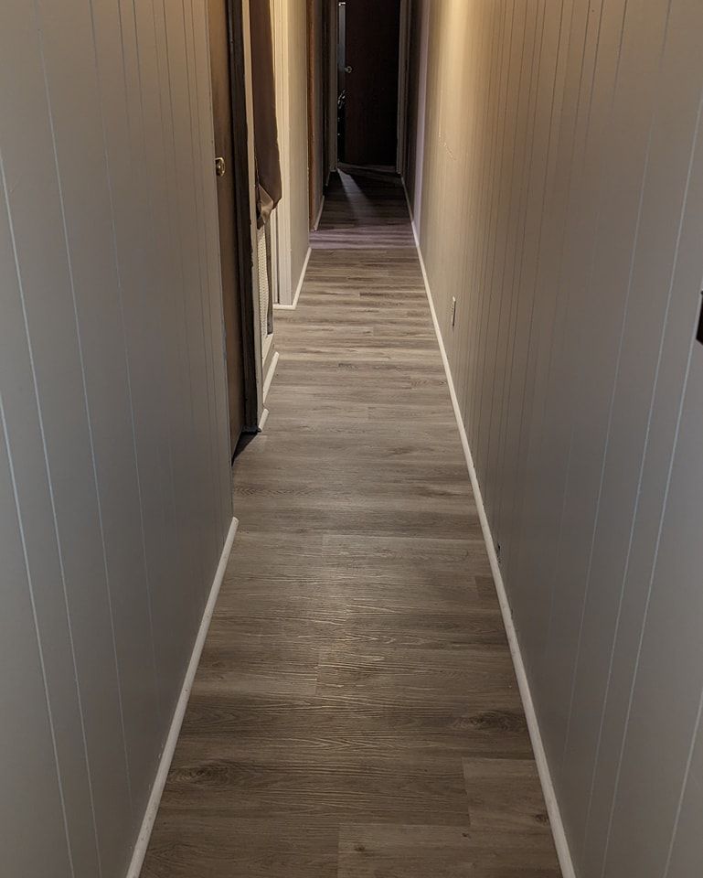 Narrow hallway with gray paneled walls, wood-look floor, and a dark doorway at the end.