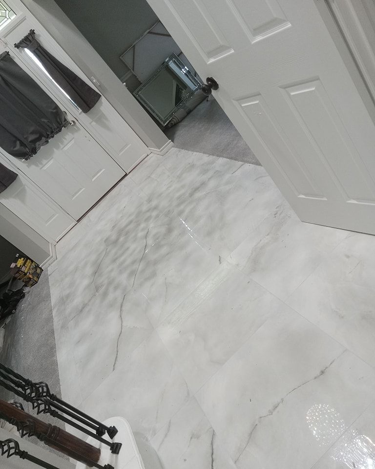 White and grey marble-look flooring in a hallway, with white doors, and a wrought iron staircase.
