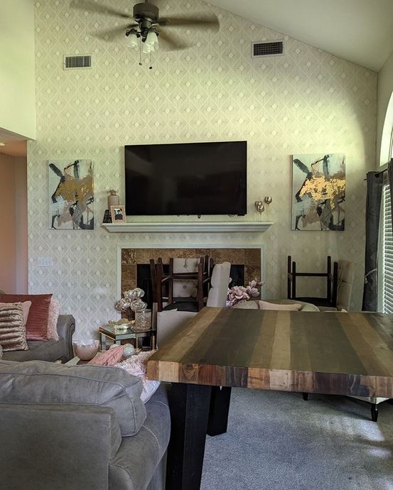 Living room with TV above fireplace, two artworks on the wall, and a large wooden table.