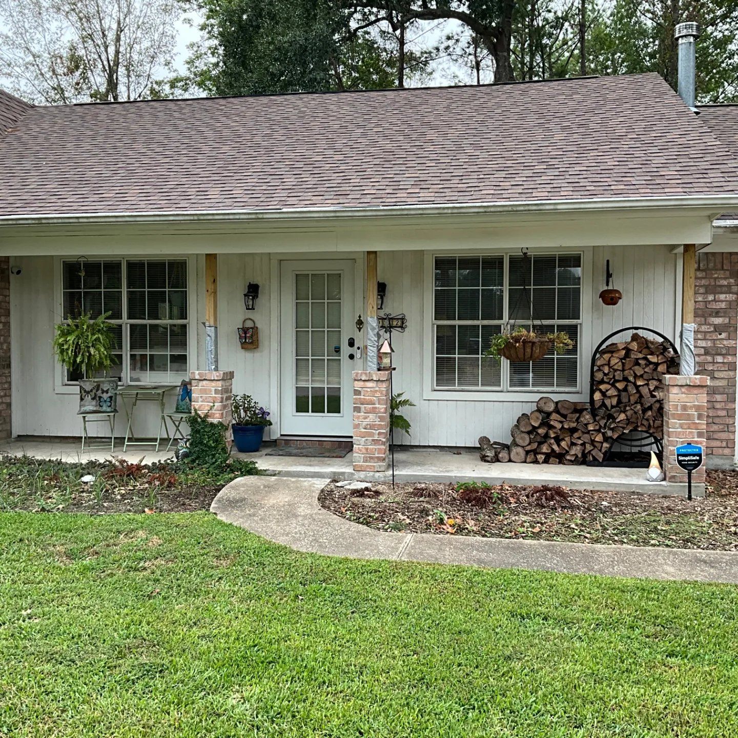 Front exterior of a white house with a brown roof and brick accents. Porch features windows, a door, and plants.