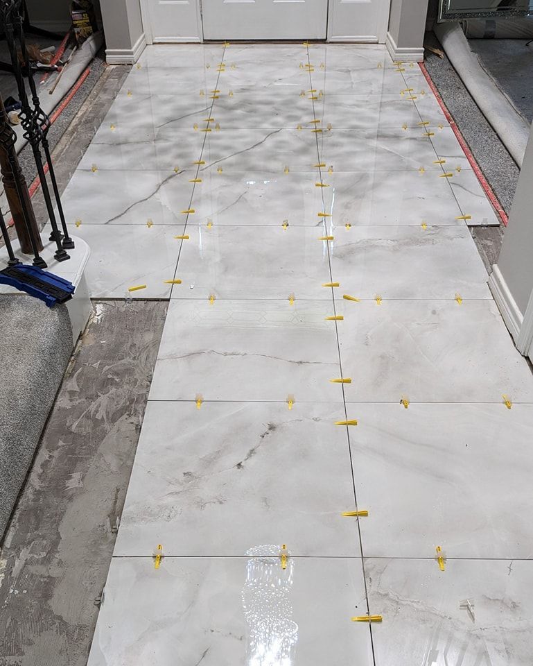 Installation of large, light-colored rectangular tiles on a floor, with yellow spacers in between, in a home.