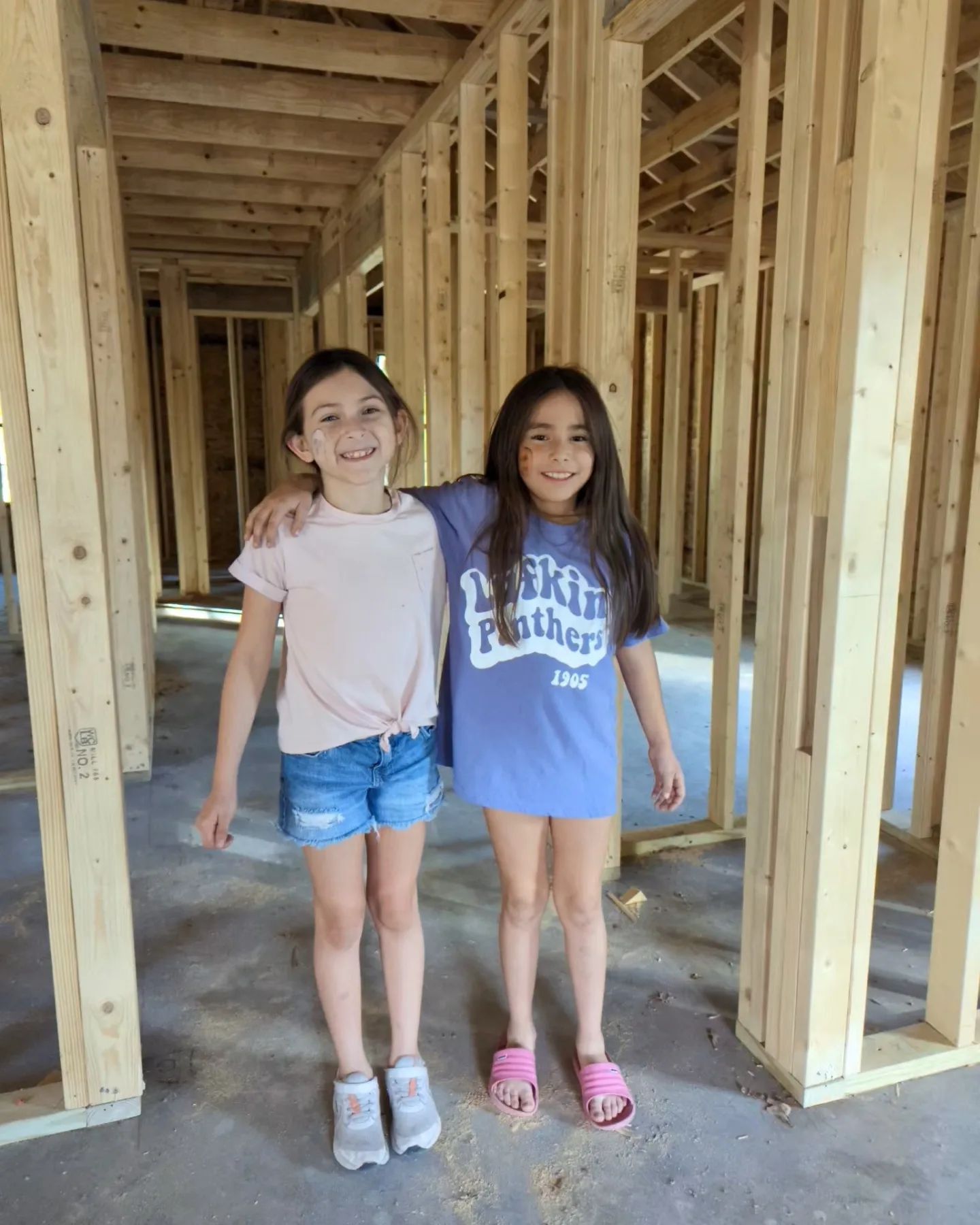 Two girls smiling and posing in a wood-framed building under construction.
