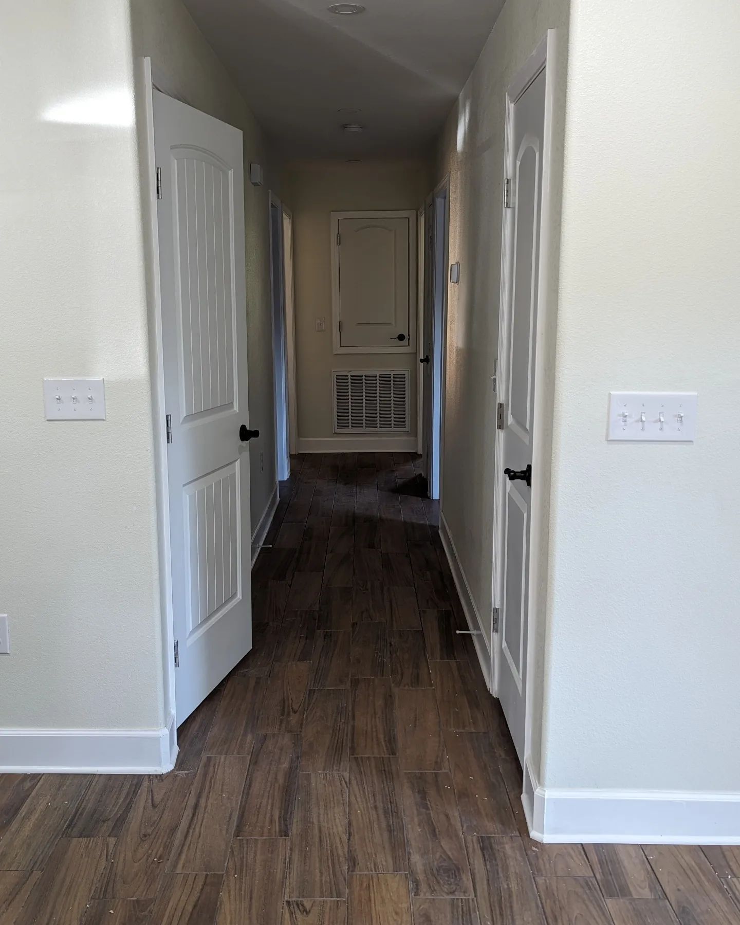 Narrow hallway with white doors, dark wood floor, and light walls.