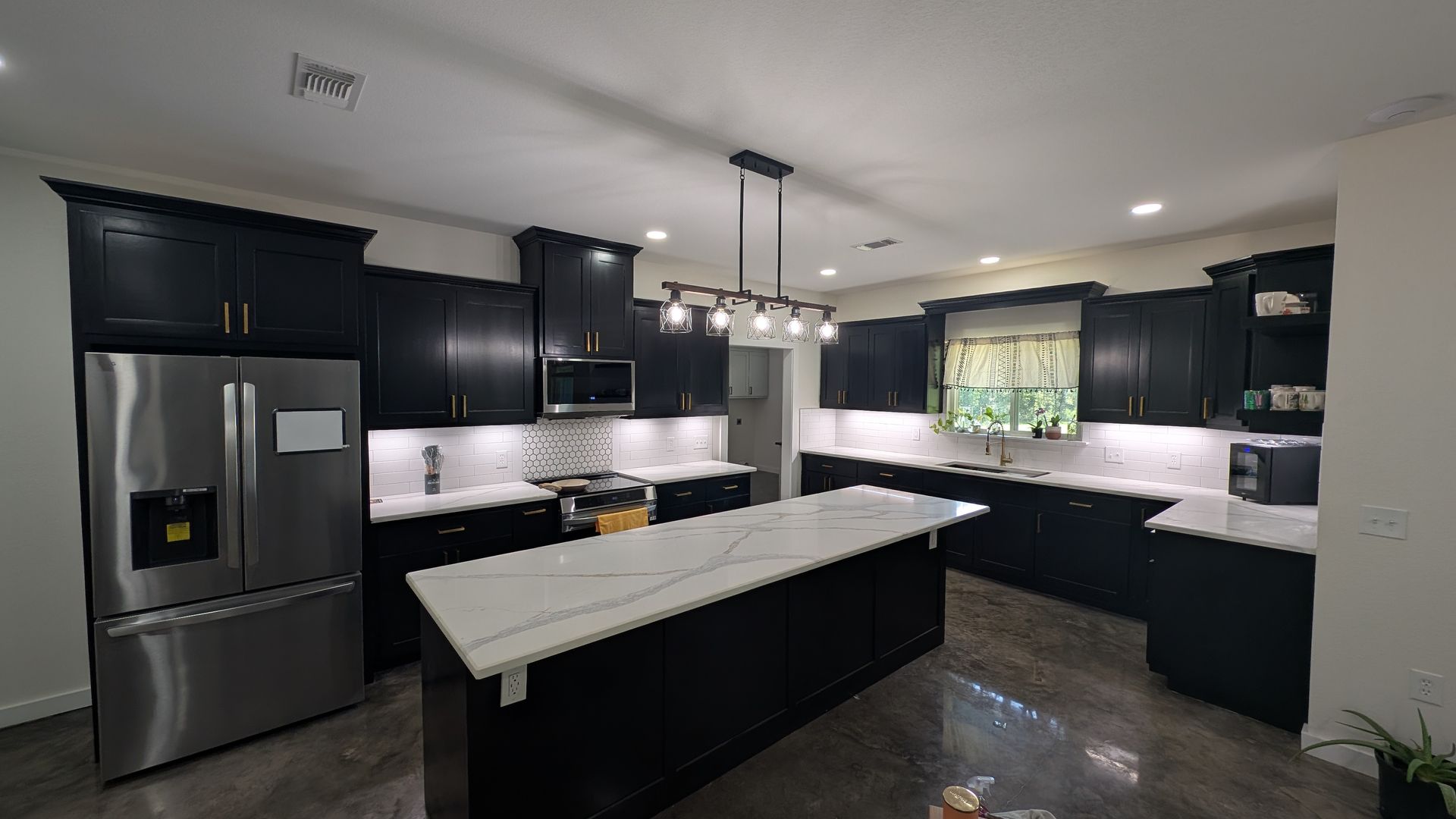 Kitchen with light green cabinets, dark countertops, white subway tile backsplash, stainless steel appliances.