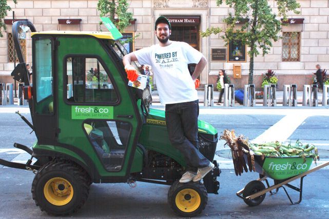 A man is standing next to a green tractor that says fresh go