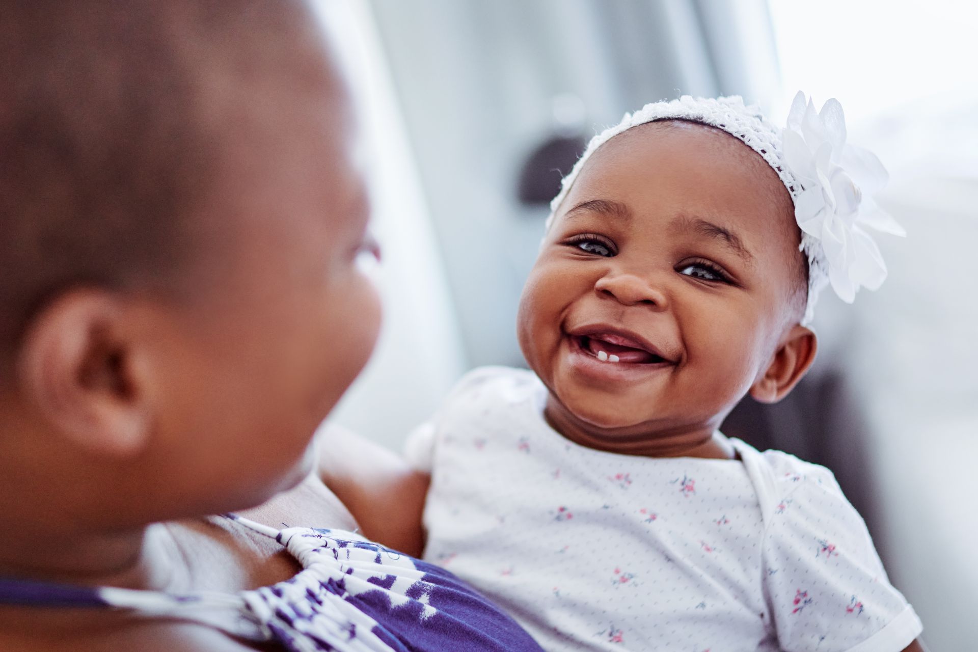 A woman is holding a baby girl in her arms and the baby is smiling.