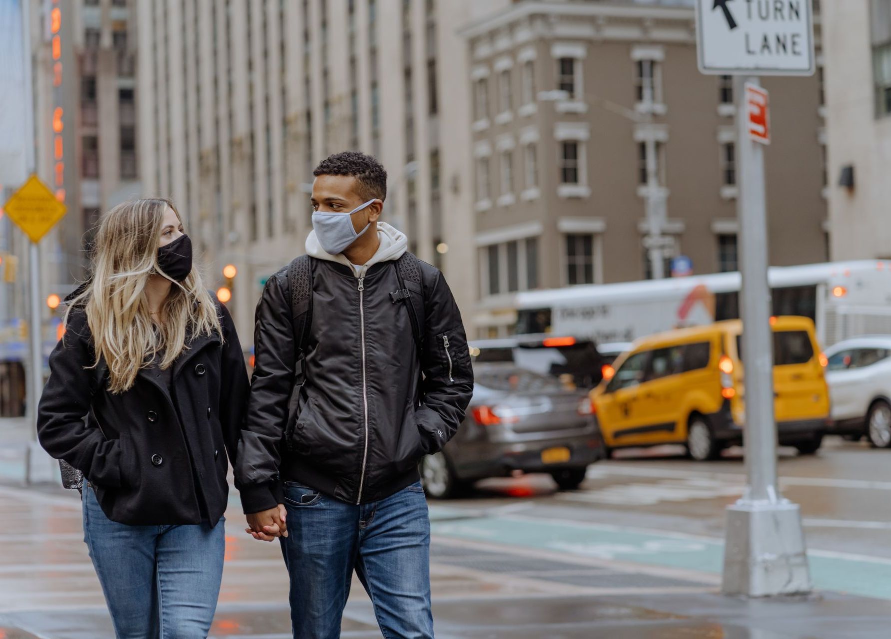 A man and a woman wearing face masks are walking down a city street.