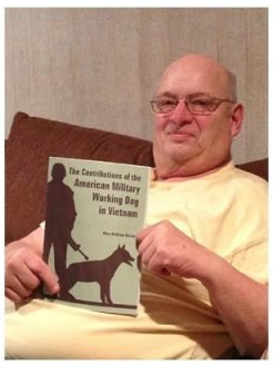 A man is holding a book titled the contributions of the american military working dog in vietnam