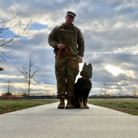 A man standing next to a black dog on a leash