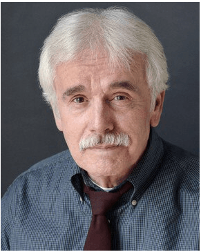 A man with gray hair and a mustache is wearing a blue shirt and tie.