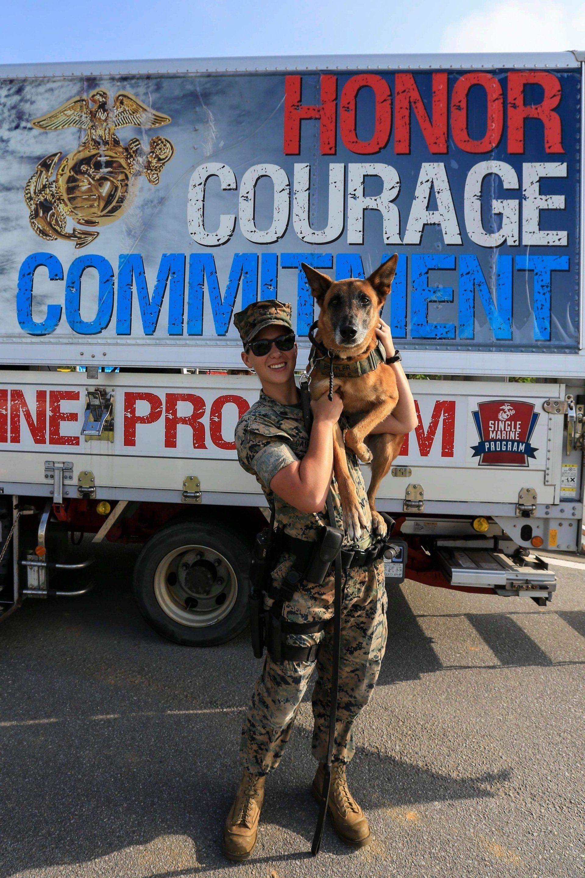 A soldier is holding a dog in front of a truck that says honor courage commitment