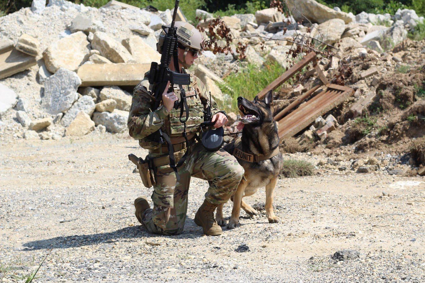A soldier is kneeling down next to a german shepherd dog.