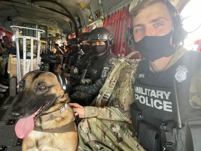 A man in a military police vest is sitting next to a dog.