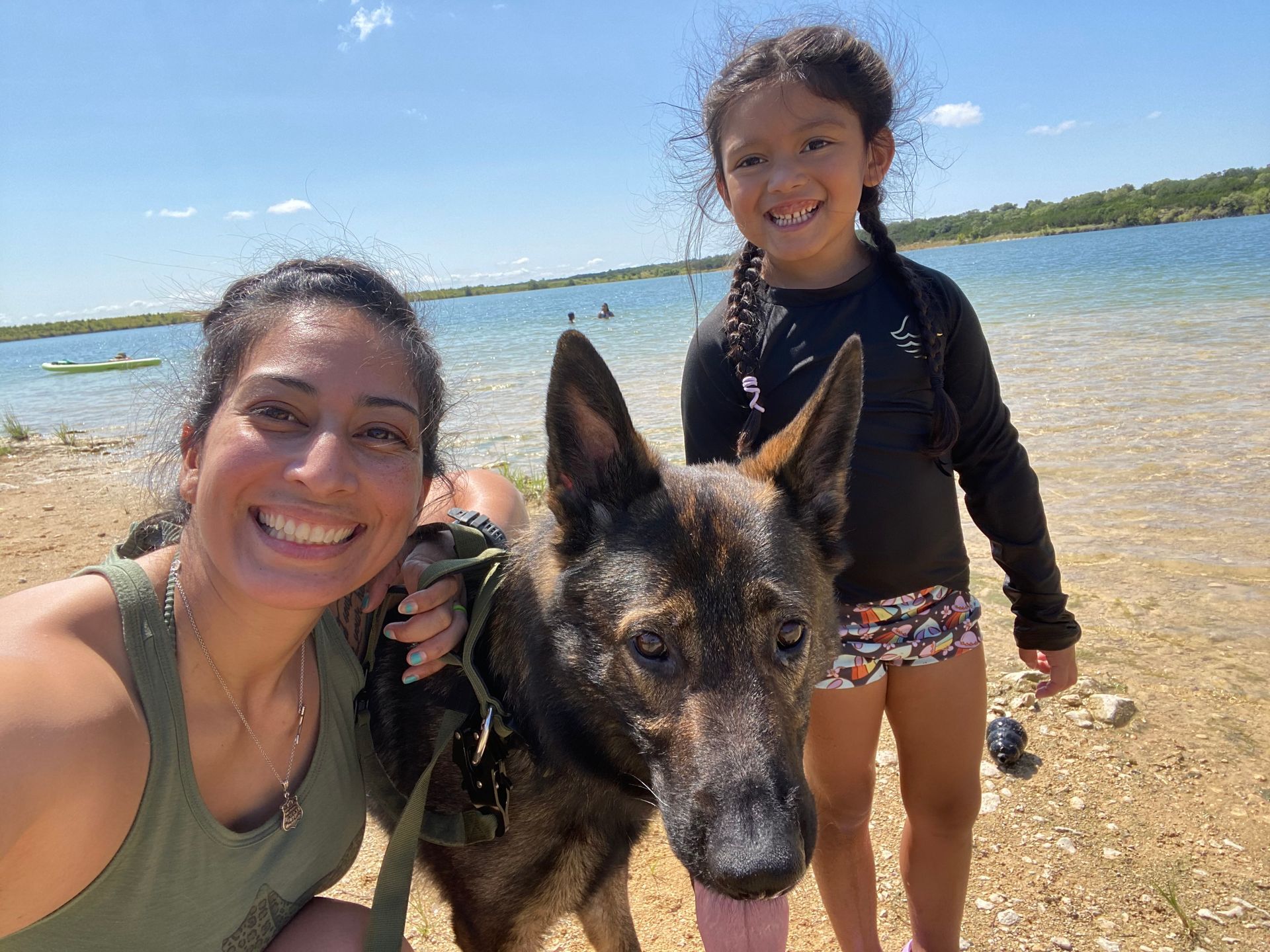 A woman and a little girl are posing for a picture with a dog on the beach.