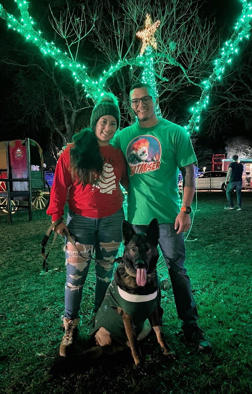A man and a woman are standing next to a dog in front of a christmas tree.