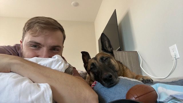 A man is laying on a bed with a dog and a basketball.