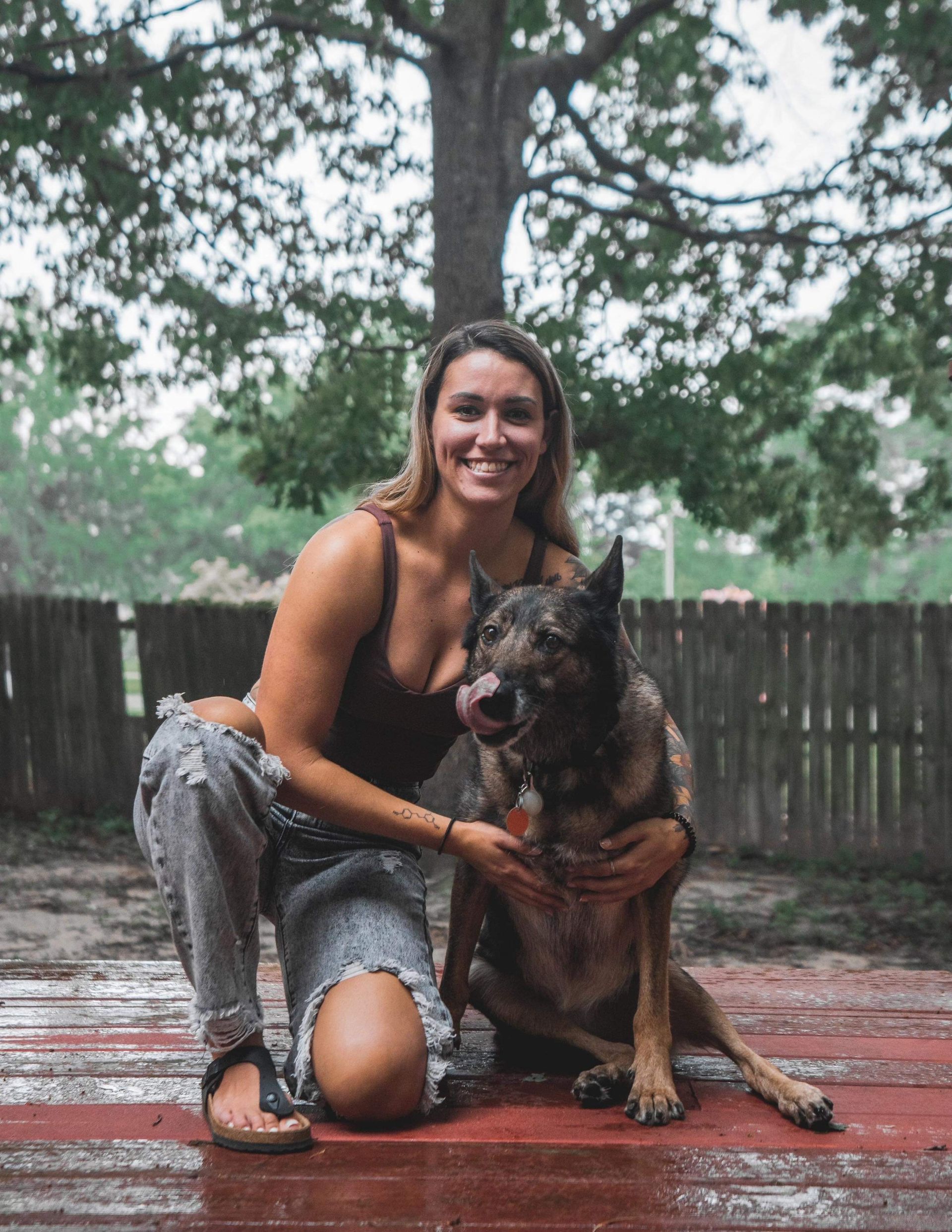 A woman is kneeling down next to a dog in the rain.