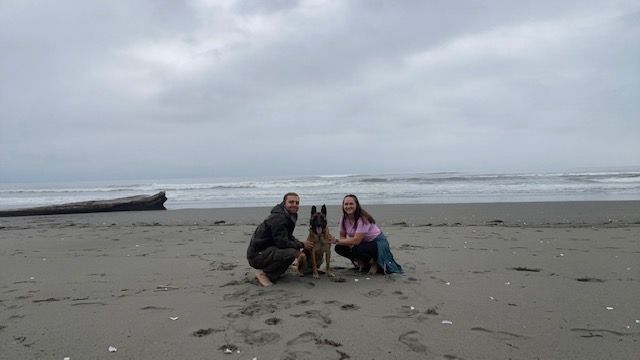 Two people and a dog are posing for a picture on the beach.