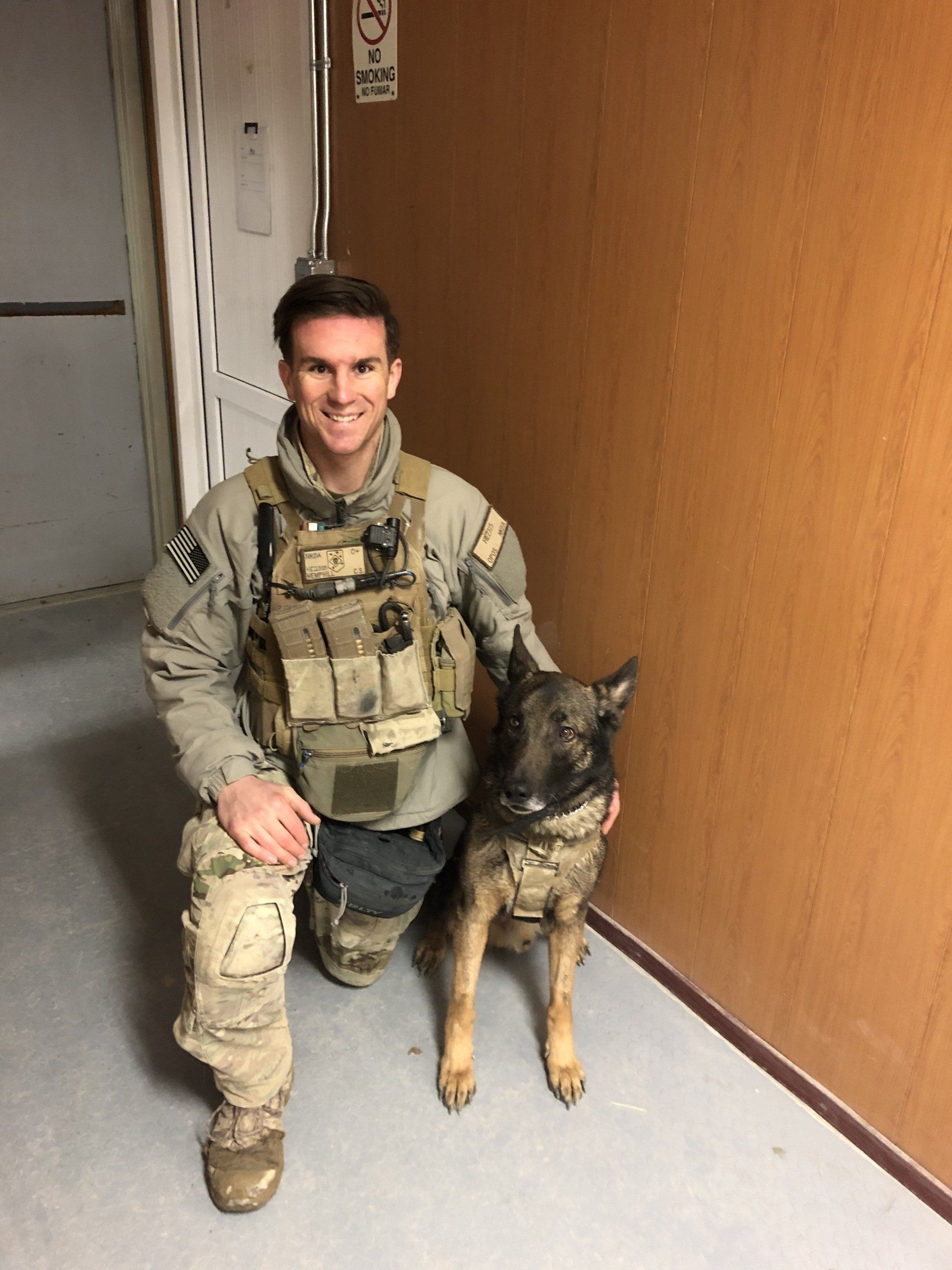 A man in a military uniform is kneeling next to a dog