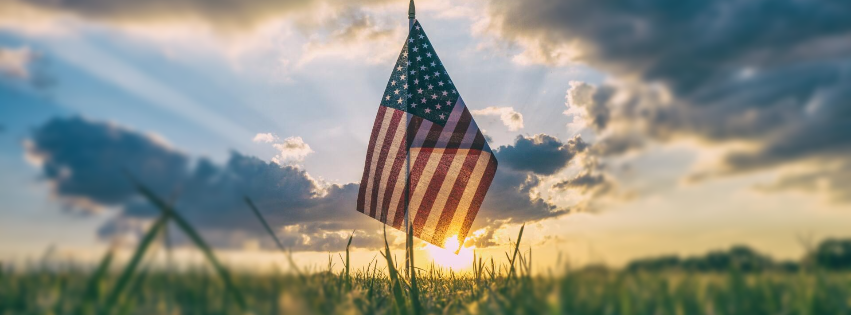 An american flag is flying in a field at sunset.