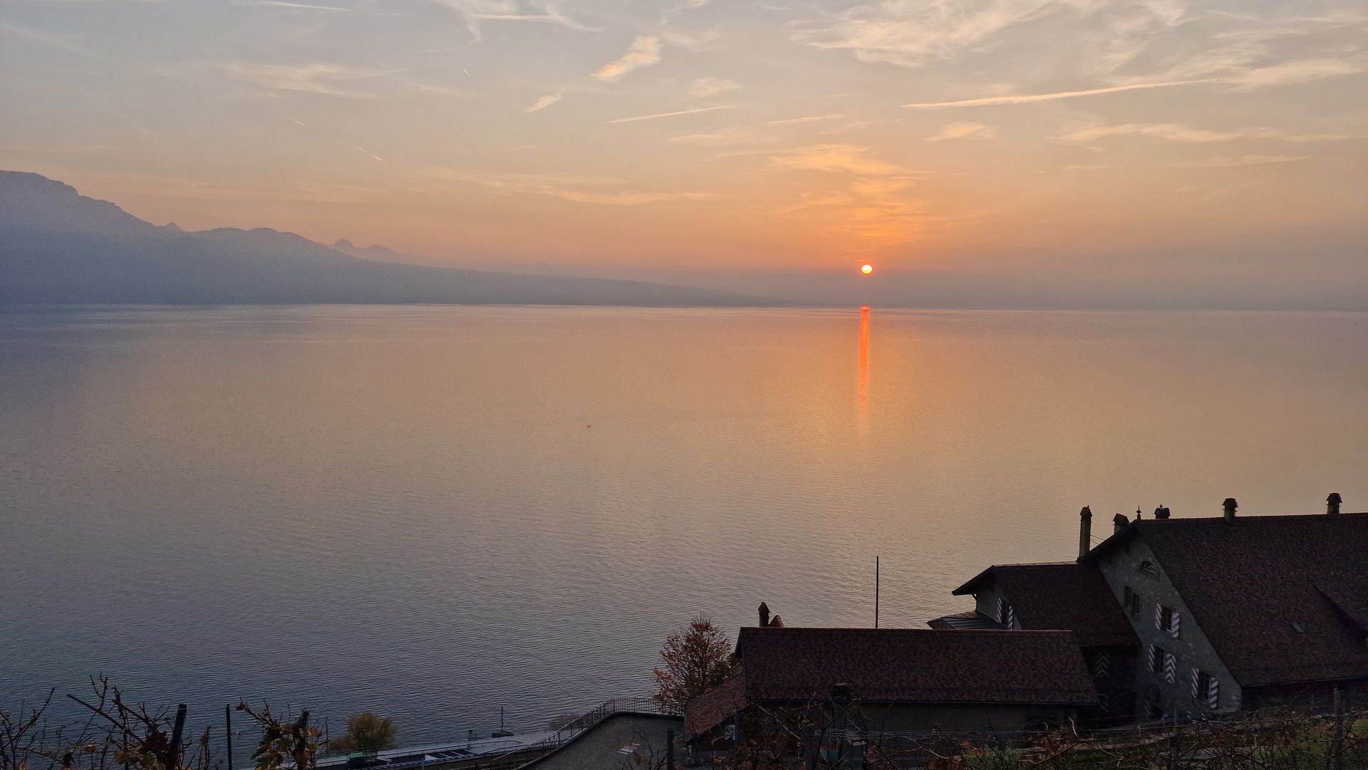 Un coucher de soleil sur une grande étendue d'eau avec des montagnes en arrière-plan.