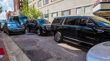 A row of black cars are parked on the side of the road in front of a building.