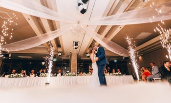 A bride and groom are kissing on the dance floor at their wedding reception.