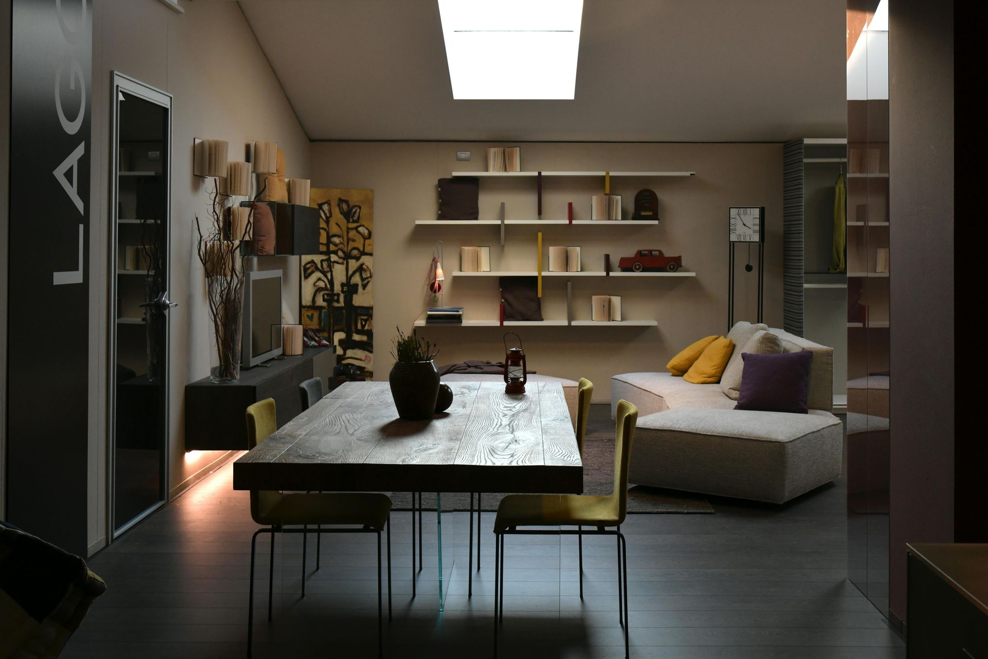 Modern living room with dining table, sofa, shelves, and warm ambient lighting