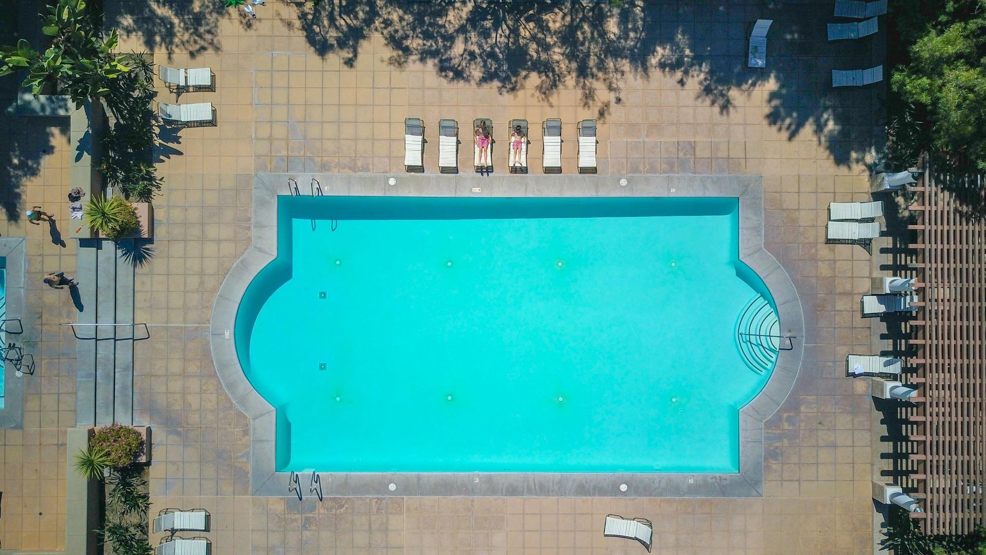 Aerial view of a turquoise swimming pool on a tiled deck with lounge chairs around it.