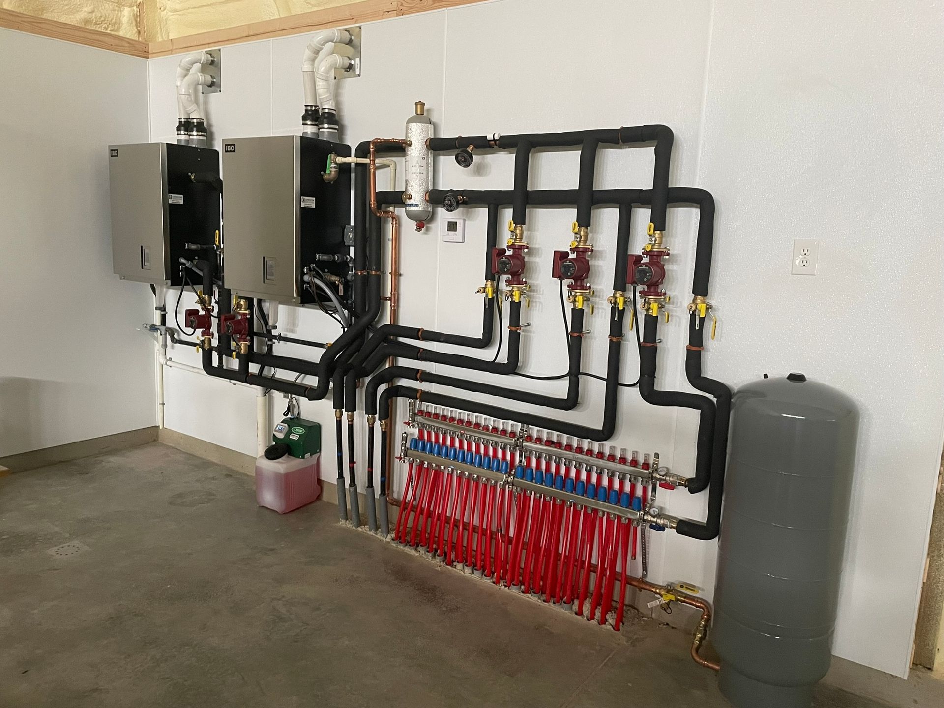 Hydronic heating system components mounted on a white wall, including boilers, pumps, and piping.