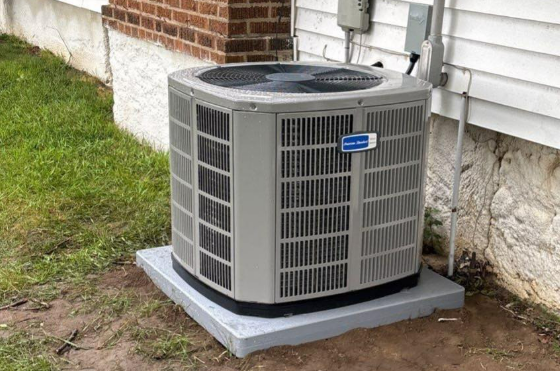 Air conditioning unit on a concrete pad next to a brick building, white siding, and green grass.