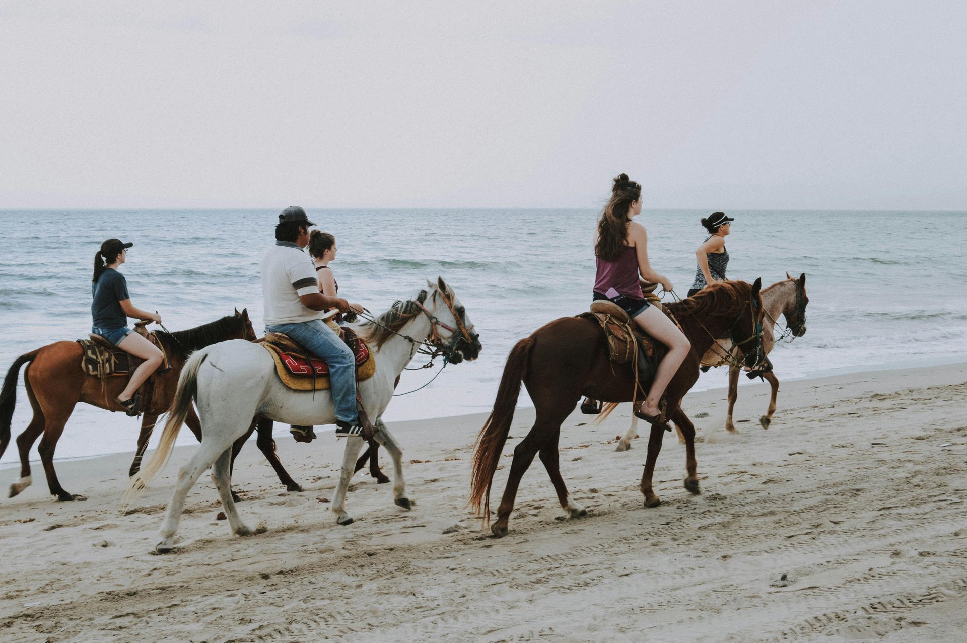 A group of people riding horses along a sandy beach near the ocean.