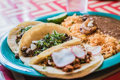 Plate of tacos, rice, and beans with sliced radishes on a teal dish