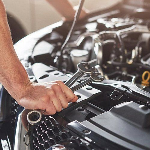 A Man Is Working On The Engine Of A Car With A Wrench — P & M Performance & Mechanical In Bungalow, QLD