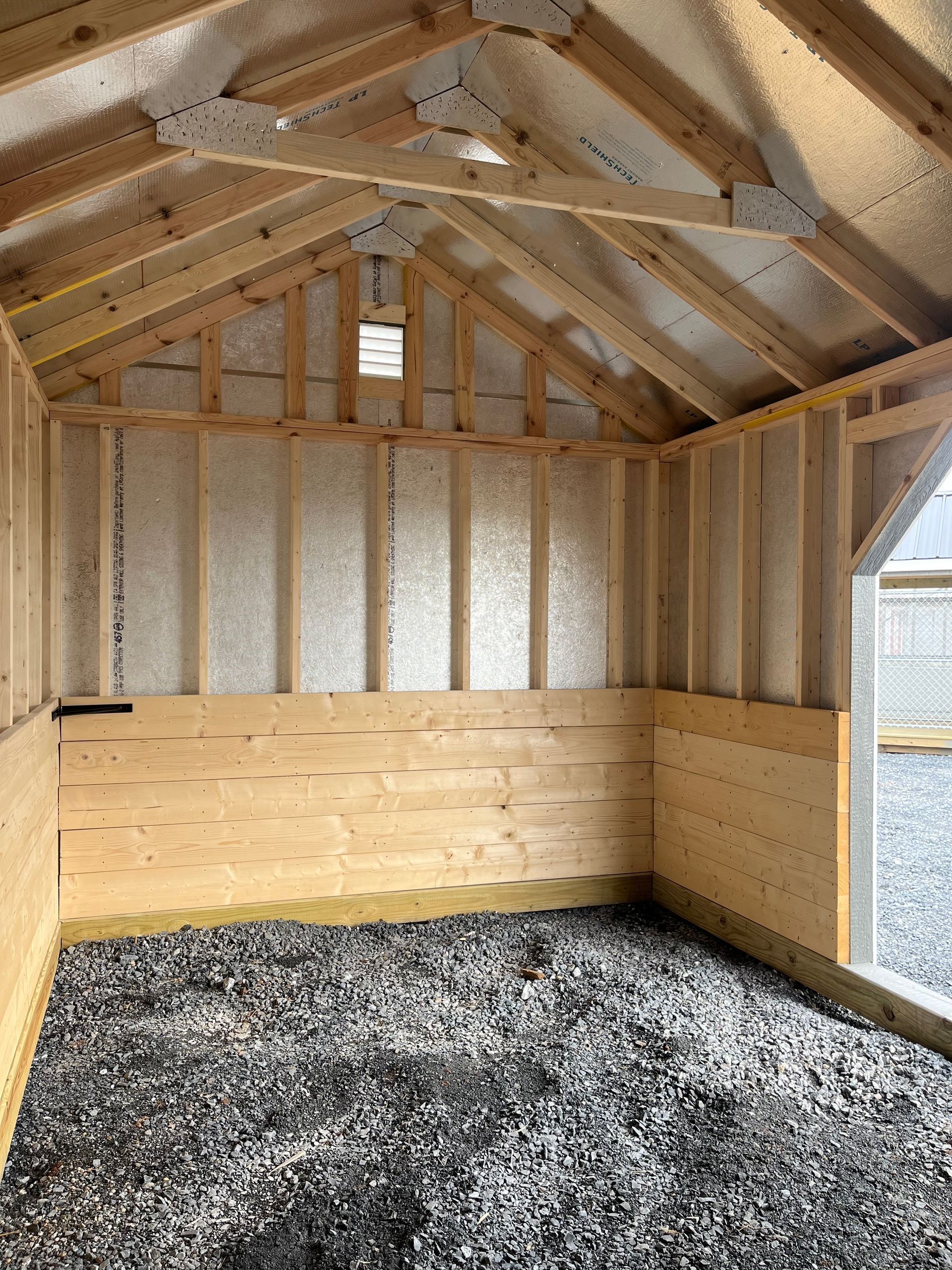 The inside of a wooden shed with gravel on the floor.