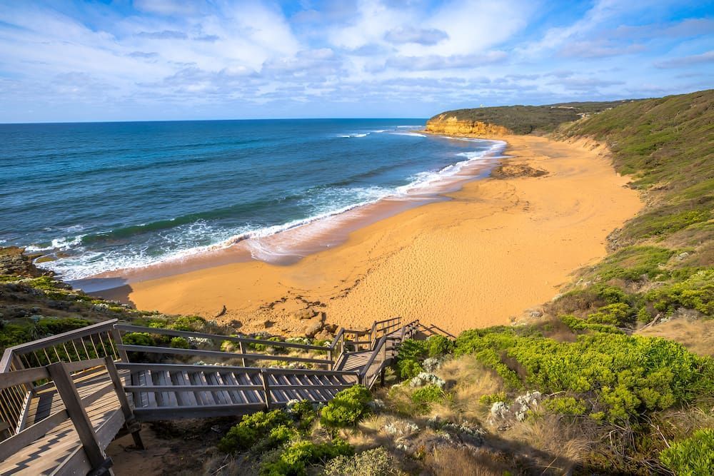 A Wooden Staircase Leading Up To A Sandy Beach Next To The Ocean — Justin Drew Plumbing in Torquay, VIC