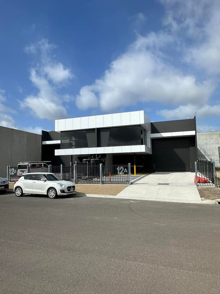 A White Car Is Parked In Front Of A Large Building — Justin Drew Plumbing in Grovedale, VIC