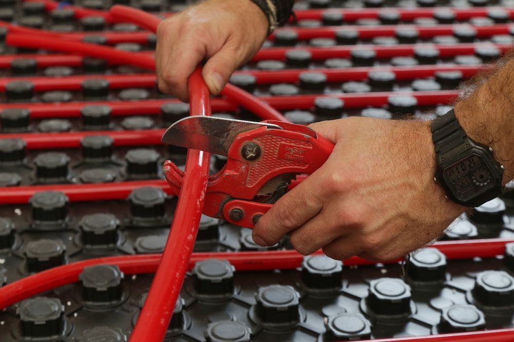 A Man Is Cutting A Red Pipe With A Pair Of Pliers — Justin Drew Plumbing in Grovedale, VIC