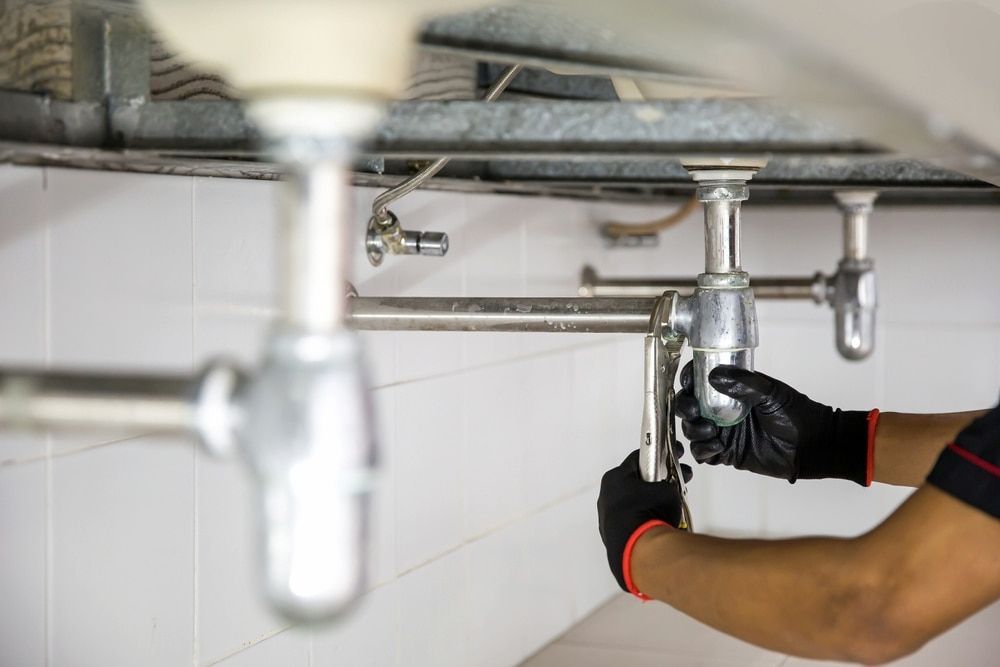 A Plumber Is Fixing A Sink Pipe In A Bathroom — Justin Drew Plumbing in Grovedale, VIC