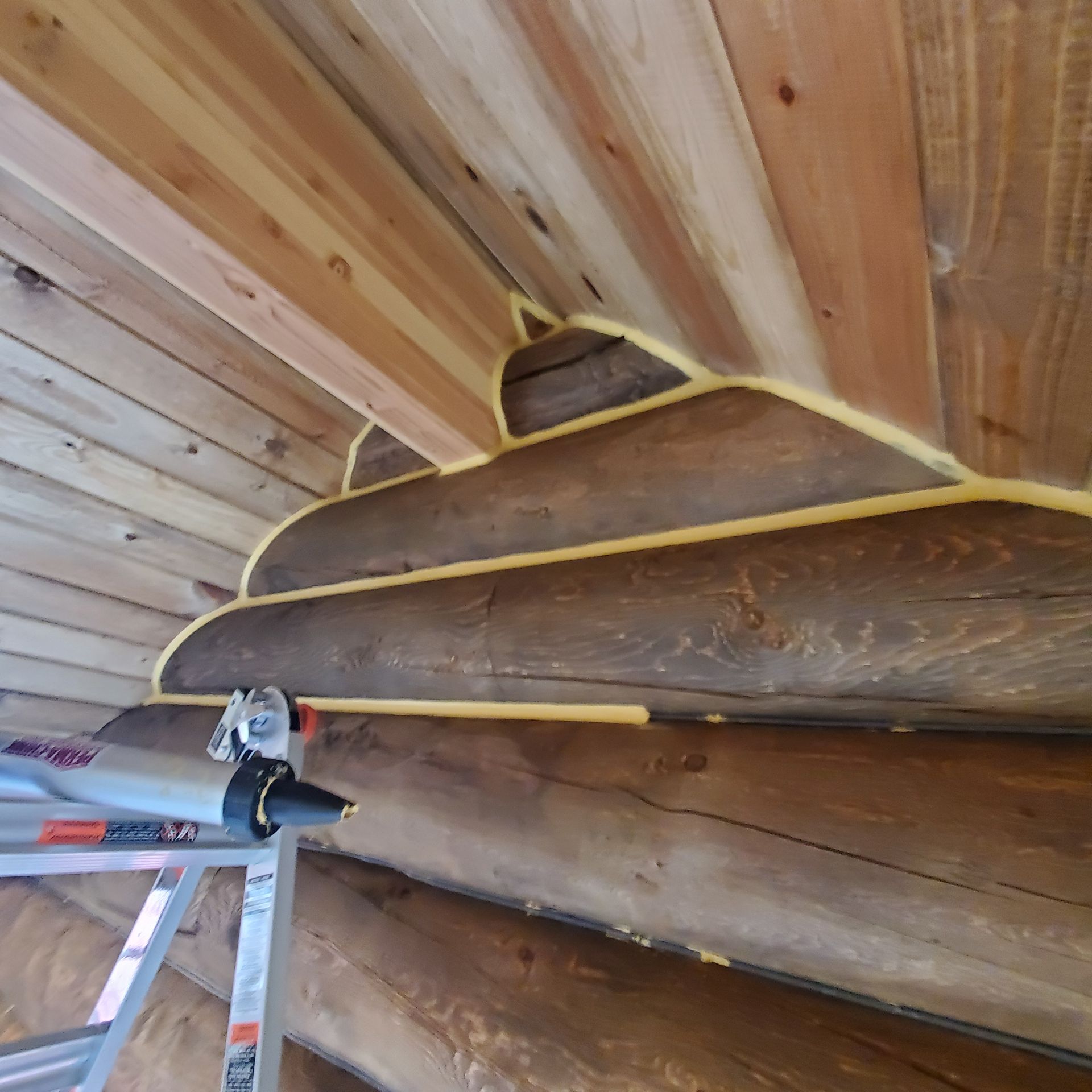 A man on a ladder is sand blasting a log cabin.