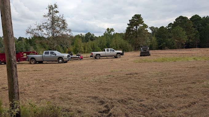 A couple of trucks are parked in a field with trees in the background.