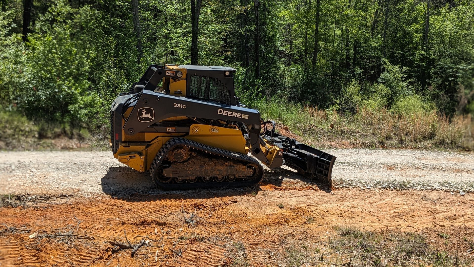 A bulldozer is driving down a dirt road in the woods.