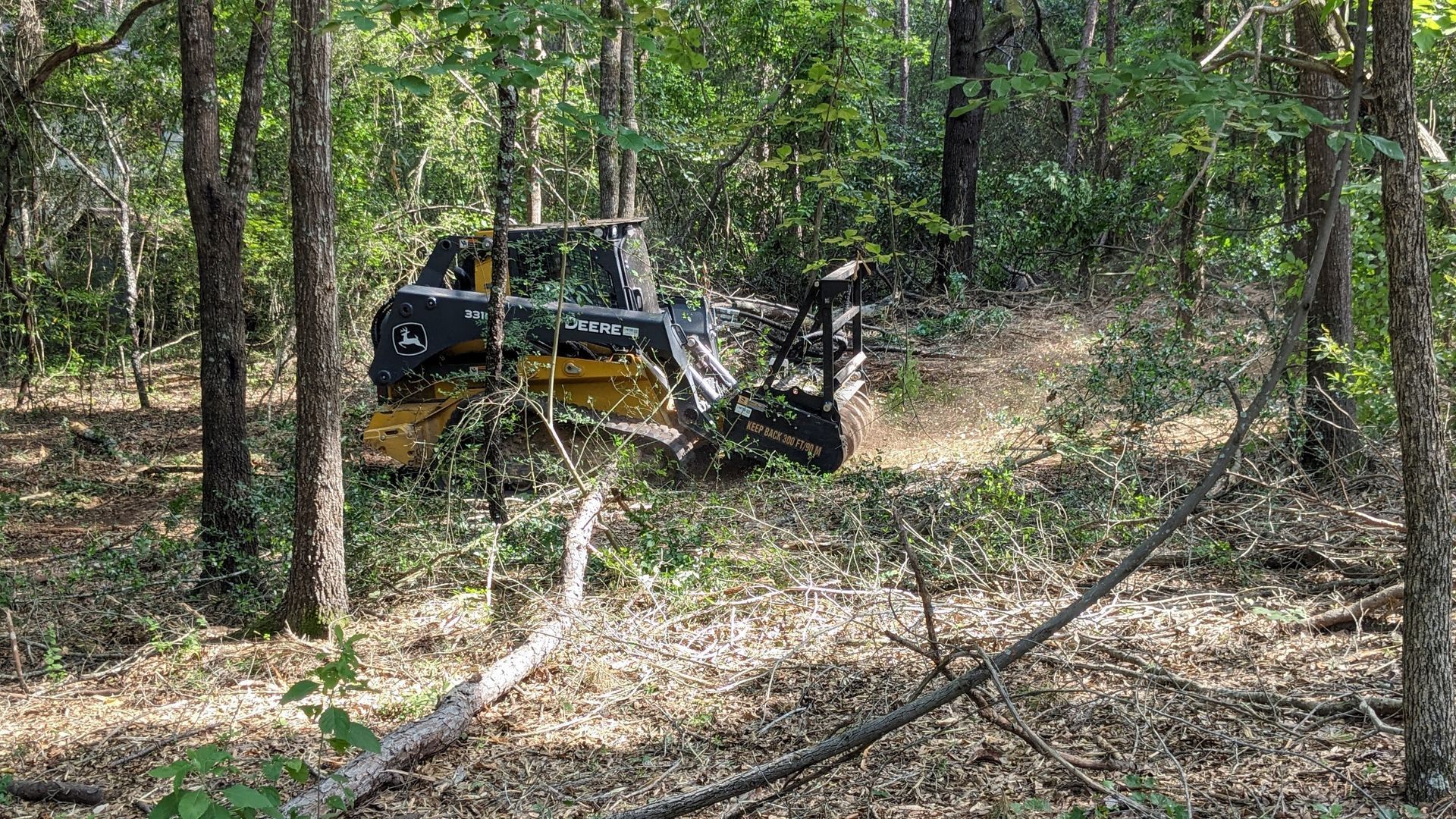 Bulldozer clearing brush in a wooded area; yellow and black vehicle.