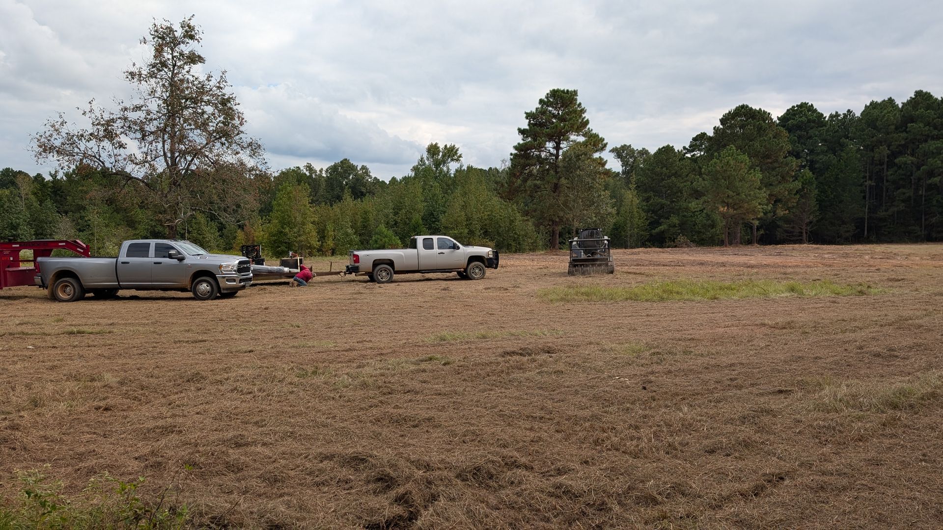 Three trucks are parked in a field with trees in the background.