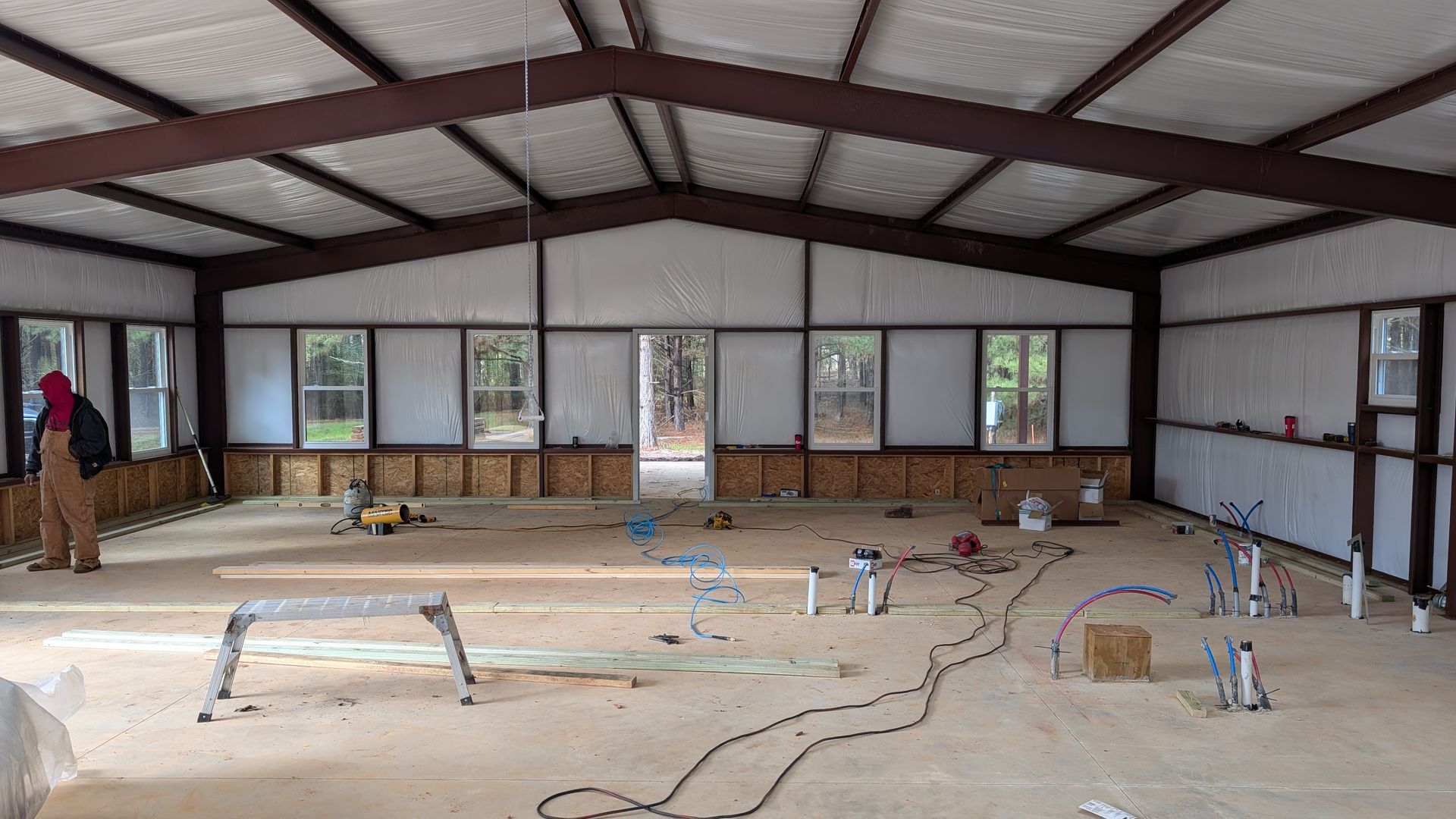Interior of a building under construction. Brown steel beams, white walls, exposed plumbing. Man working.