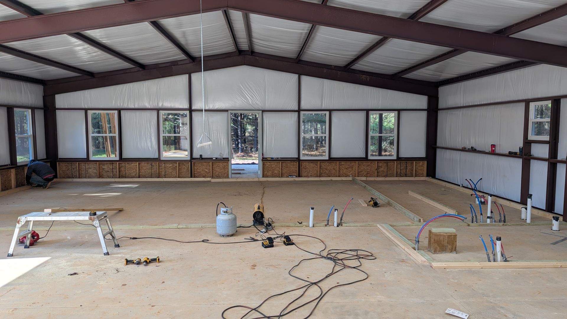 Interior of a metal building under construction, showing framing, windows, and tools on the concrete floor.