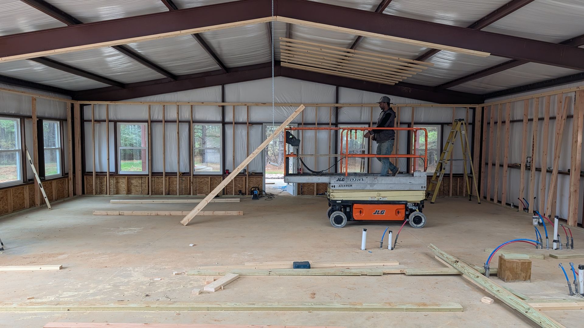 Interior of a building under construction, with a person on a lift, framing walls and ceiling.
