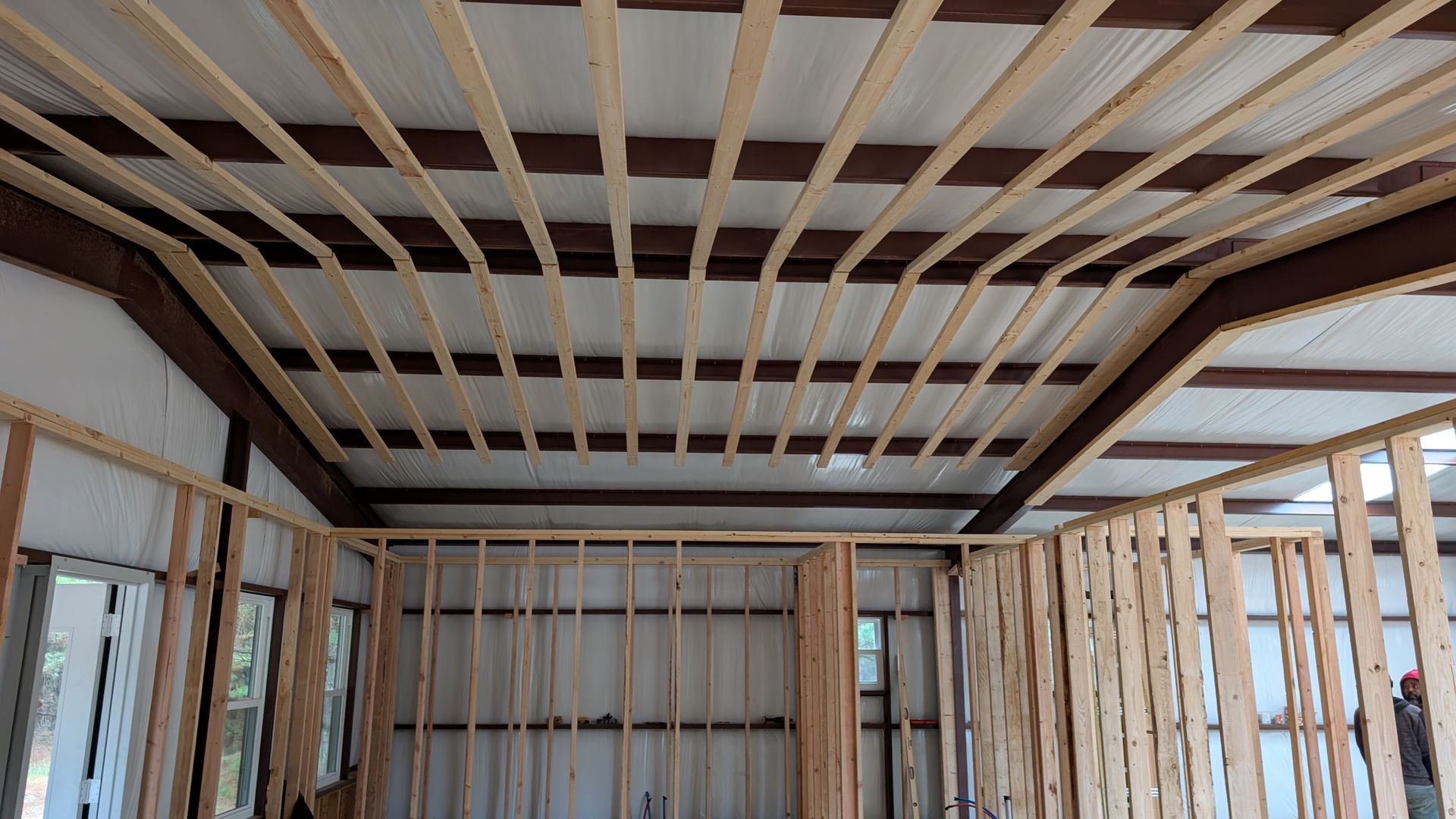 Interior view of a building under construction, showing wooden framing for walls and ceiling, against corrugated metal.