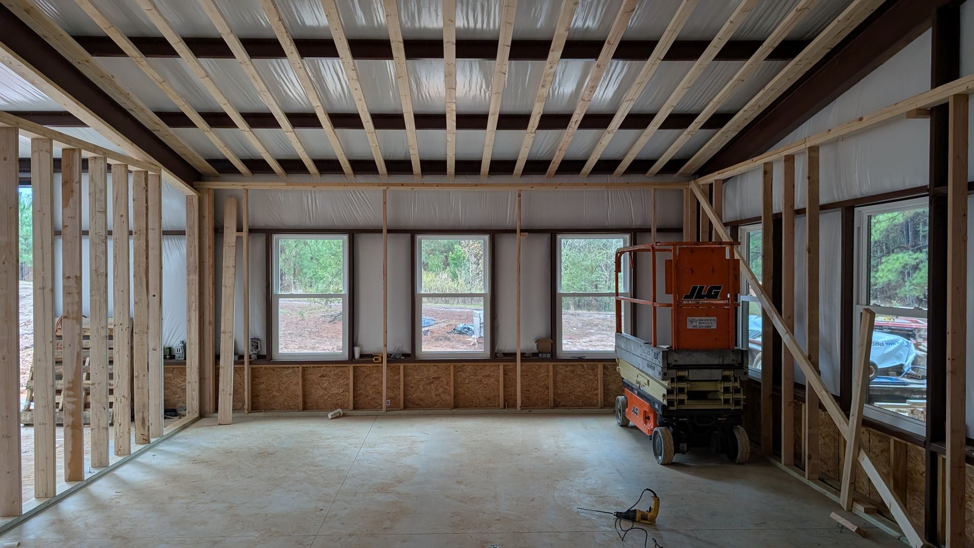 Interior of a room under construction, with wood-paneled walls and ceiling. Windows and a doorway are visible.