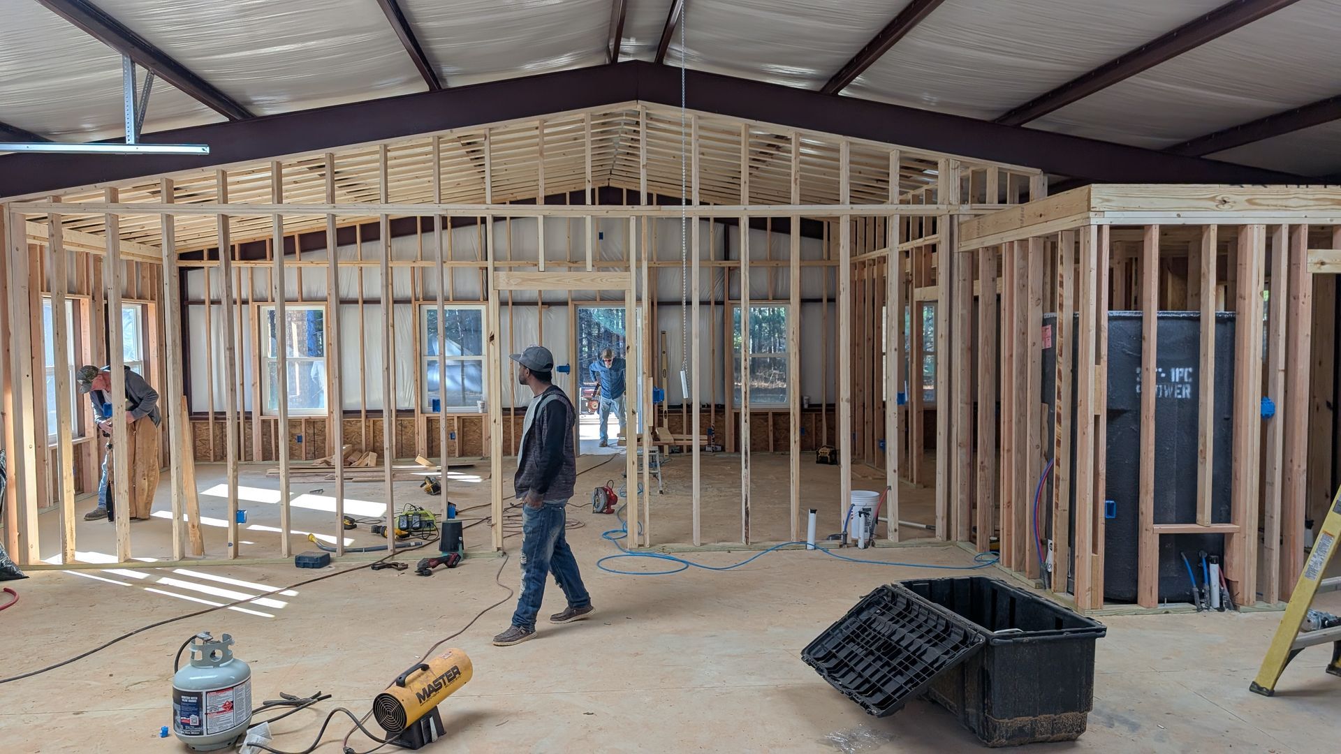 Interior of a building under construction, wooden frames, workers, tools, bare floor, natural light.
